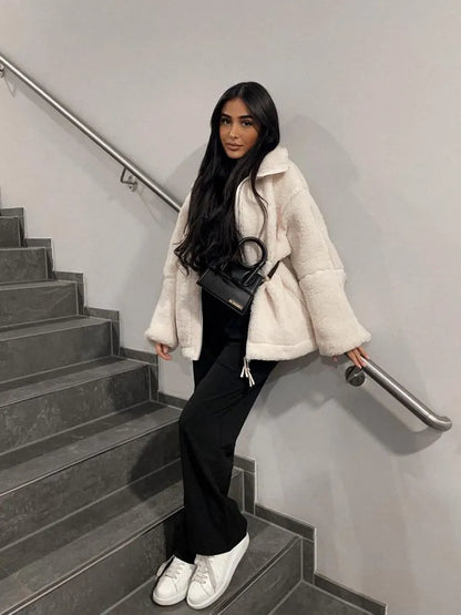 Frau in weißem Kunstpelzmantel, schwarze Hose, weiße Sneaker, schwarze Umhängetasche auf Treppe.