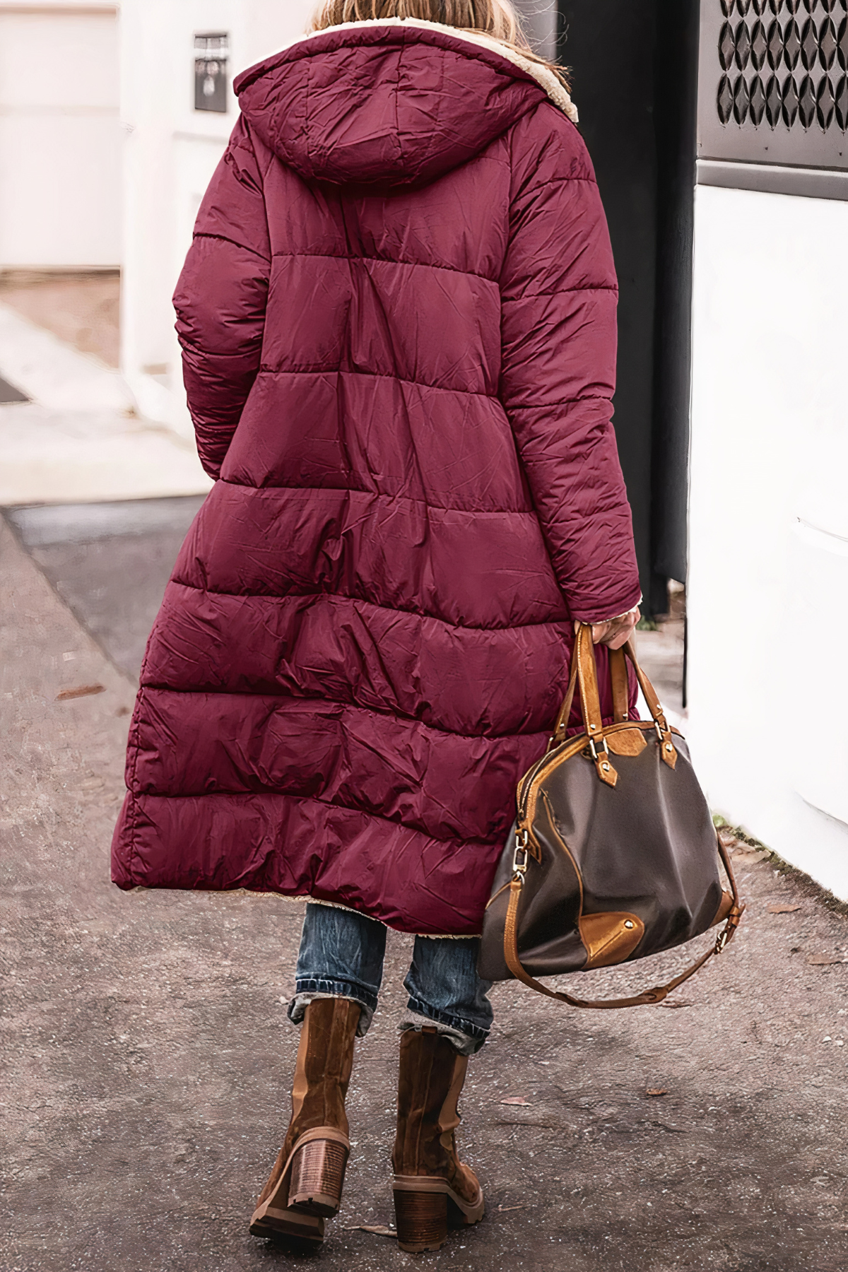 Frau in rotem Daunenmantel mit Kapuze, braune Stiefel, braune Ledertasche, Straße im Hintergrund.