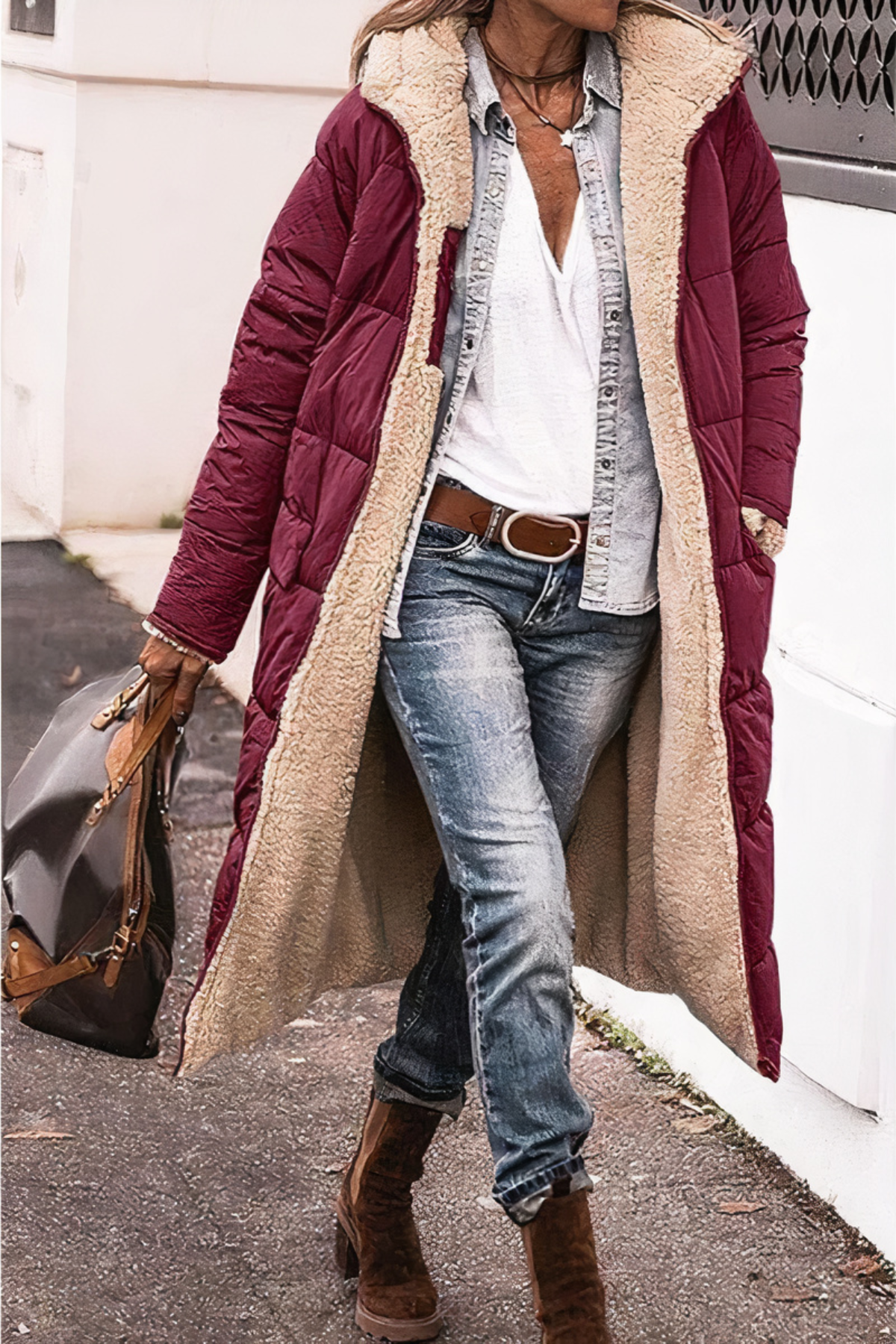 Frau in rotem Daunenmantel mit Lammfellfutter, Jeans und Stiefeln, trägt braune Ledertasche.