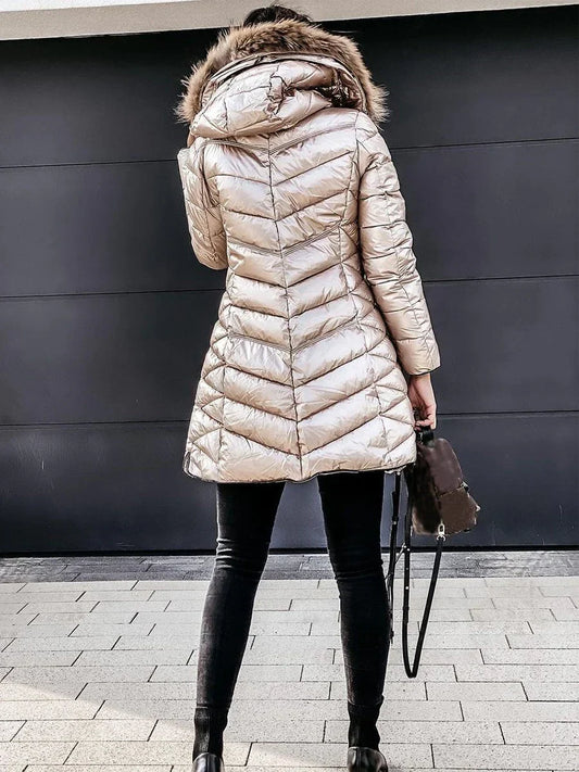 Frau in goldener Daunenjacke mit Kapuze, schwarze Hose, Handtasche, Wintermode.