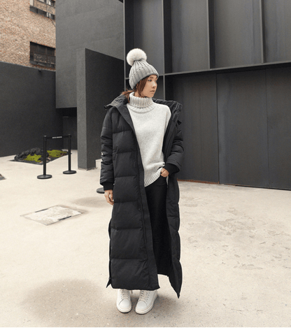 Frau im schwarzen, übergroßen Parka, Wintermantel, grauer Pullover, weiße Mütze, urbaner Hintergrund.