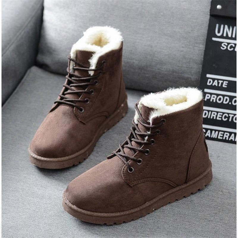 Braune Winterstiefel aus Wildleder mit weißem Kunstfellfutter auf grauem Sofa.