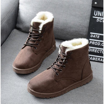 Braune Winterstiefel aus Wildleder mit weißem Kunstfellfutter auf grauem Sofa.