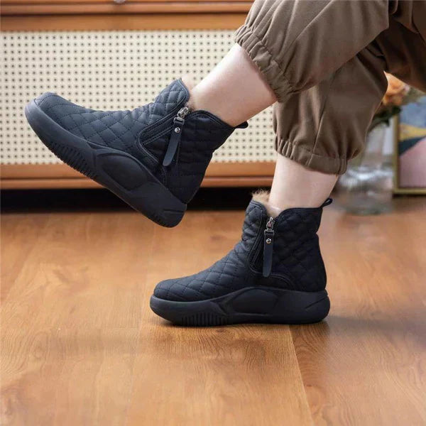 Schwarze, gesteppte Damen-Winterstiefel mit Reißverschluss auf Holzboden.