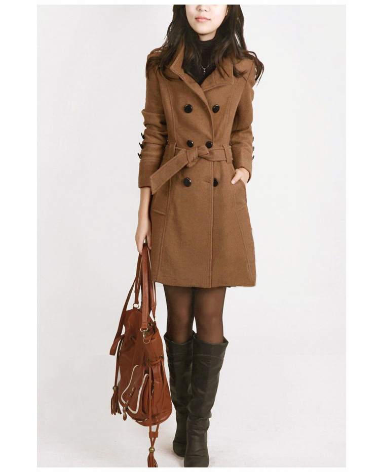 Frau in braunem Wollmantel mit Gürtel, hält braune Ledertasche, trägt schwarze Stiefel.