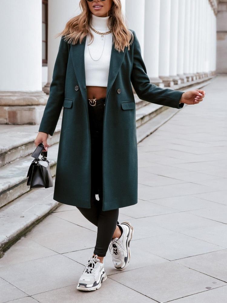 Frau in grünem Mantel, weißem Rollkragenpullover, schwarze Hose, Sneakers, Handtasche.