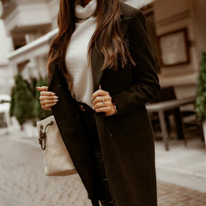 Frau in schwarzem Mantel und weißem Rollkragenpullover, hält beige Handtasche, Stadtstraße.