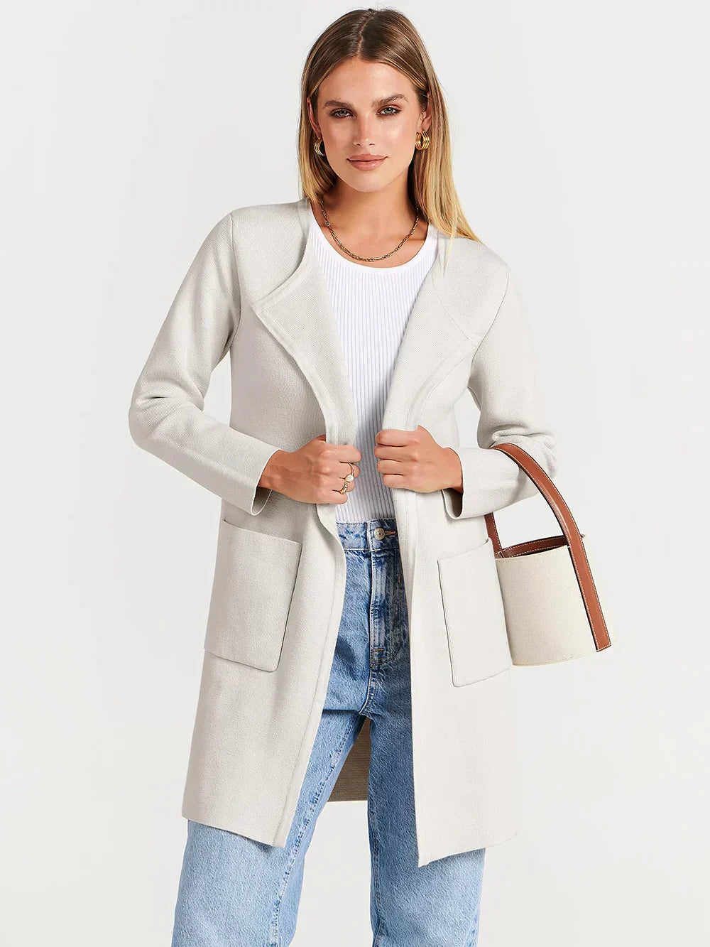 Frau in weißem Mantel und blauer Jeans mit weißer Tasche, modisch, elegant, Herbstmode.