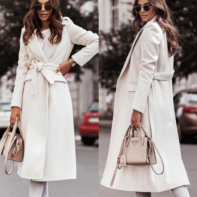 Frau in elegantem, weißem Wollmantel mit Gürtel, Sonnenbrille und beiger Handtasche.
