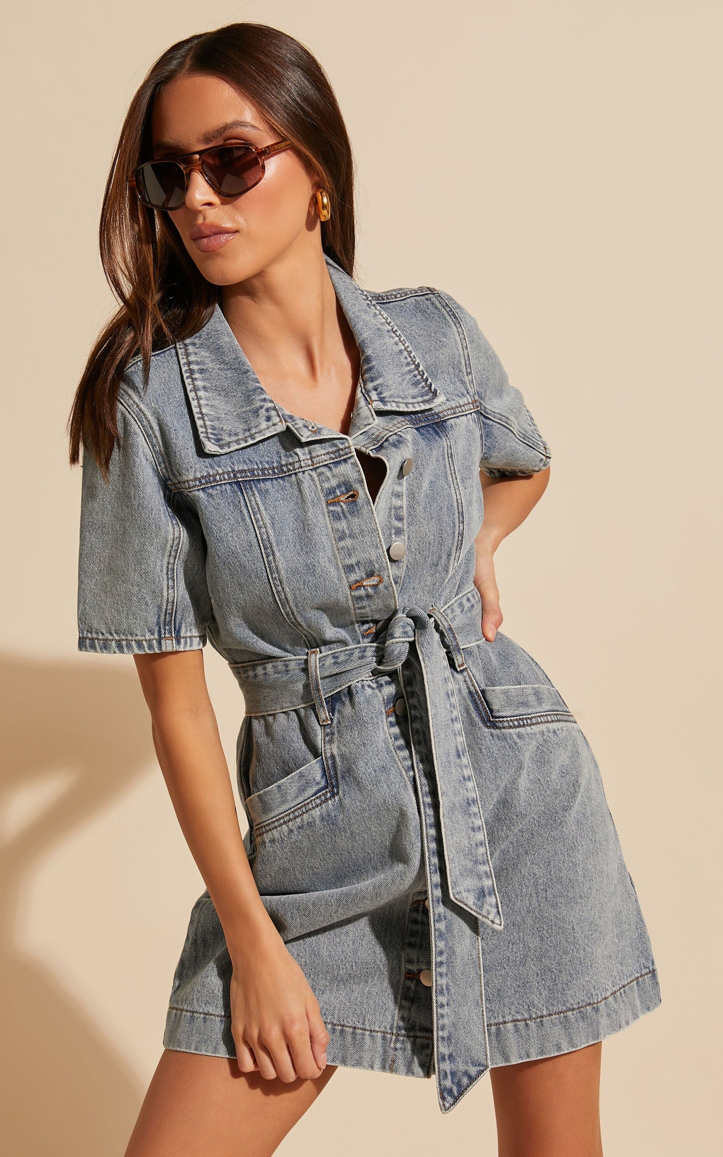Frau in blauem Jeanskleid mit Knopfleiste und Gürtel, Sonnenbrille, modisch, lässig.