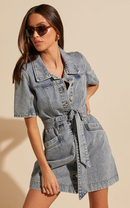 Frau in blauem Jeanskleid mit Knopfleiste und Gürtel, Sonnenbrille, modisch, lässig.