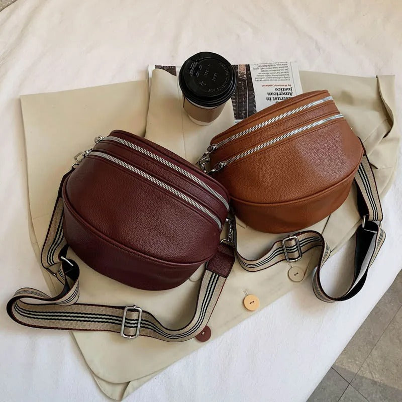 Zwei Leder-Gürteltaschen in Braun und Rotbraun mit gestreiften Trägern auf weißem Hintergrund.