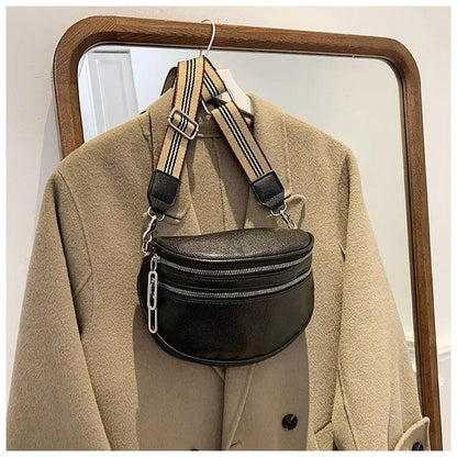 Schwarze Leder-Gürteltasche mit gestreiftem Riemen, hängend an beigem Mantel vor Spiegel.