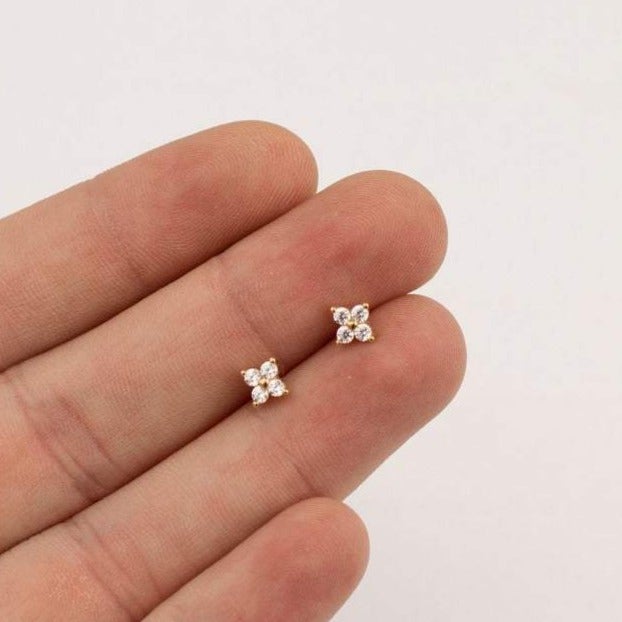 Zwei kleine, funkelnde Diamant-Ohrstecker in Blumenform auf einer Hand, eleganter Schmuck.