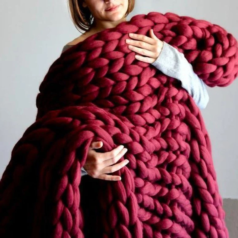 Frau mit großer, roter, grob gestrickter Decke aus Wolle, gemütlich, handgefertigt, Wohnaccessoire.