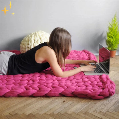 Frau auf pinker, grob gestrickter Decke arbeitet am Laptop, gemütliches Wohndesign.