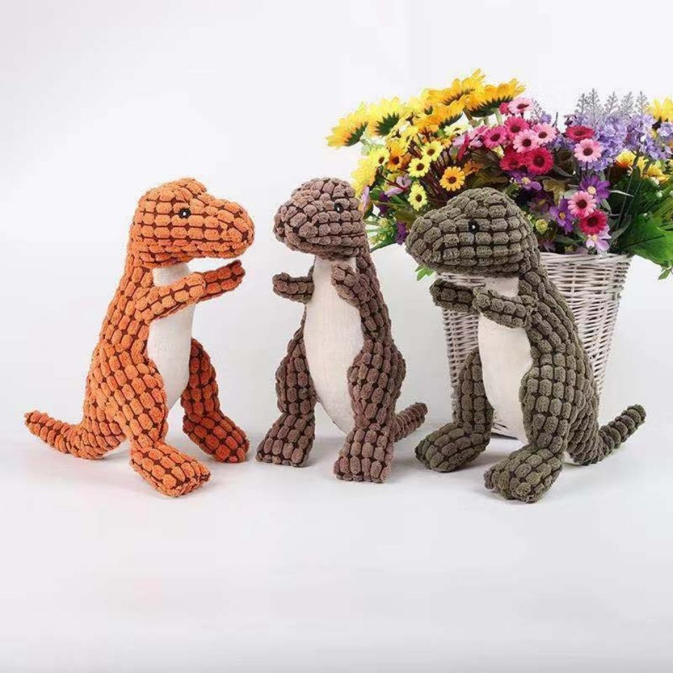 Drei gehäkelte Dinosaurier-Spielzeuge vor einem Korb mit bunten Blumen.