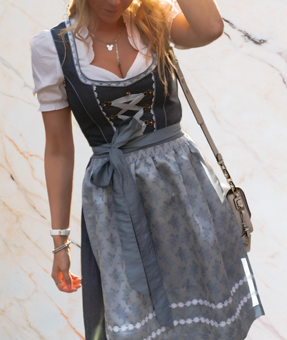 Frau in traditionellem blauen Dirndl mit weißer Bluse und grauer Schürze, Oktoberfestmode.