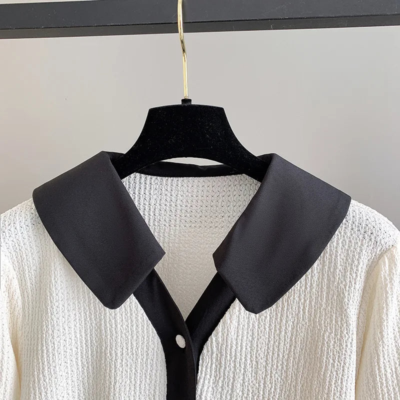 Weiße Strickbluse mit schwarzem Kragen, elegantes Design, Damenmode, hängend auf Bügel.