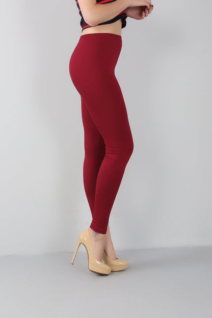 Frau in roten Leggings und beigen High Heels vor grauem Hintergrund.