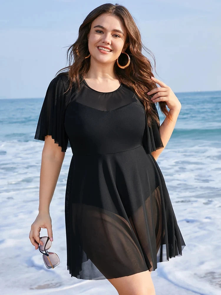 Frau im schwarzen Strandkleid am Meer, Plus-Size, Sommermode, lächelnd, mit Sonnenbrille.