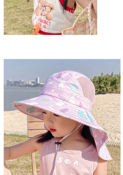 Mädchen mit lila Sonnenhut mit Hasenmotiv am Strand, Sommermode, Kinderbekleidung.