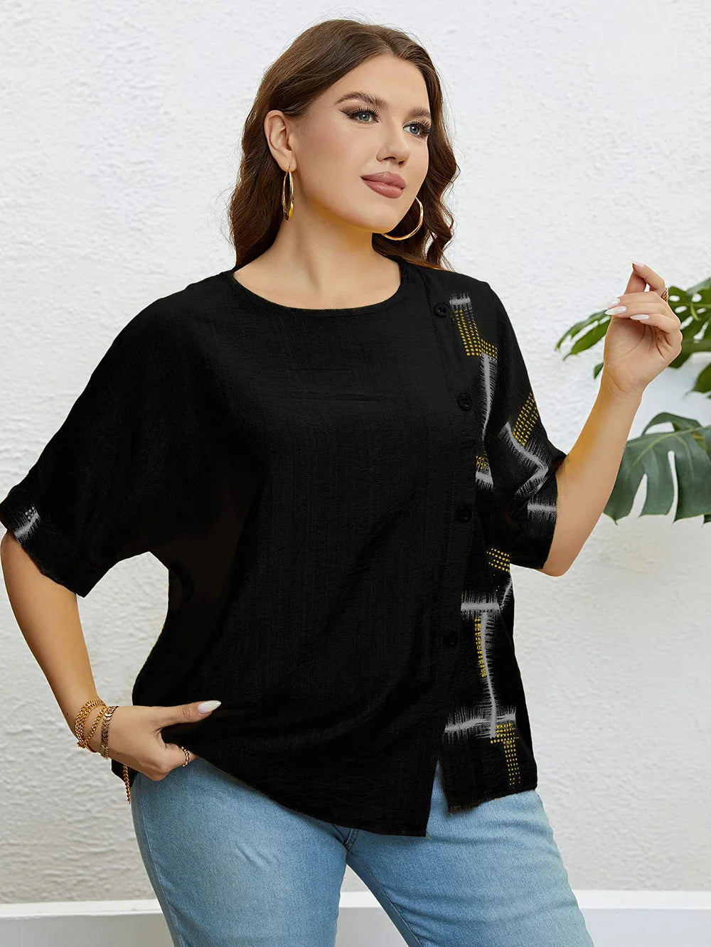 Frau in schwarzer Bluse mit Knöpfen und Muster, blaue Jeans, goldene Ohrringe, lässige Mode.