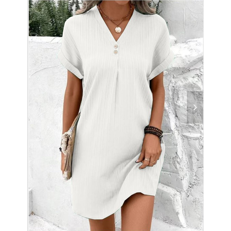 Frau in weißem Sommerkleid mit V-Ausschnitt und Knöpfen, lässiger Stil, draußen stehend.