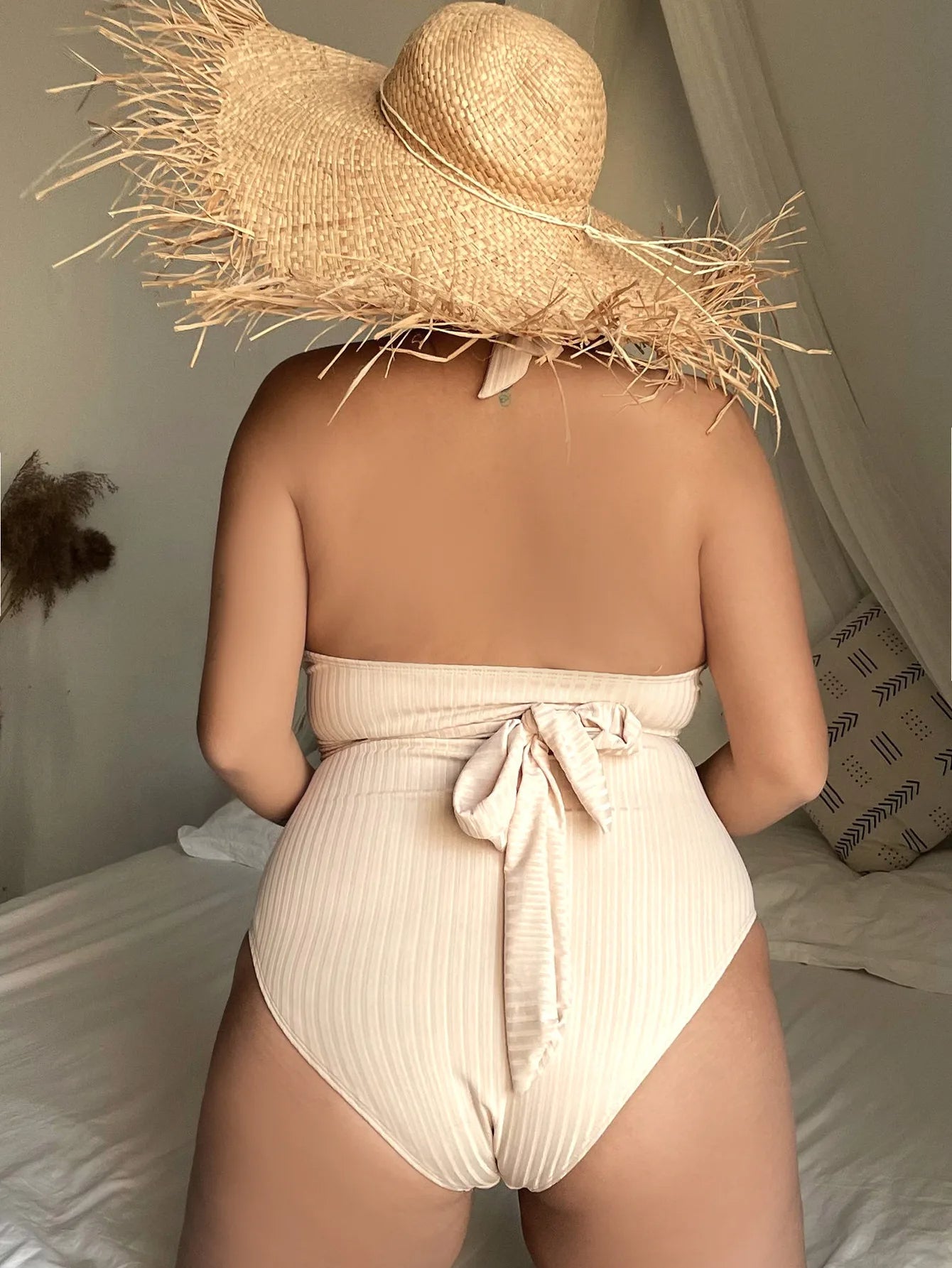 Frau im cremefarbenen Badeanzug mit Strohhut auf Bett, Sommermode, Strandkleidung.