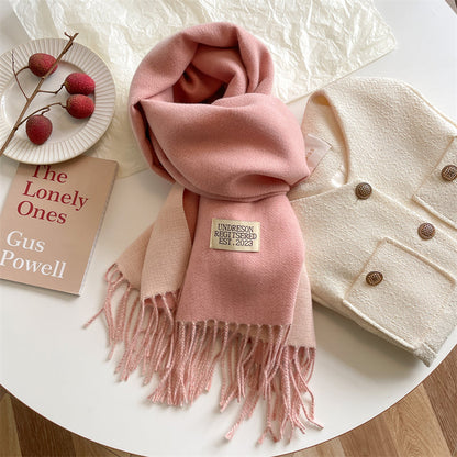 Rosa Wollschal mit Fransen auf Tisch, neben weißer Jacke und Buch, stilvolles Winteraccessoire.