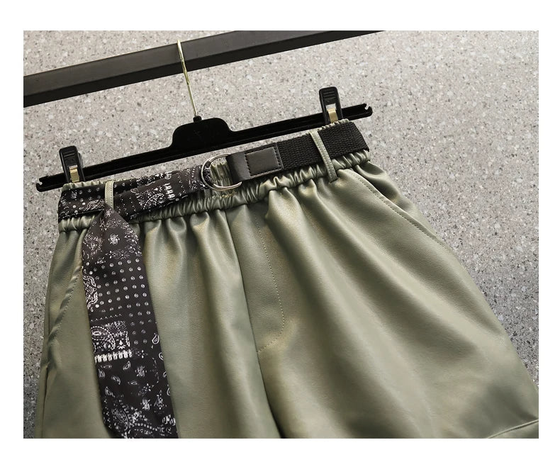 Grüne Lederhose mit schwarzem Gürtel und gemustertem Schal, Damenmode, elegant und modern.
