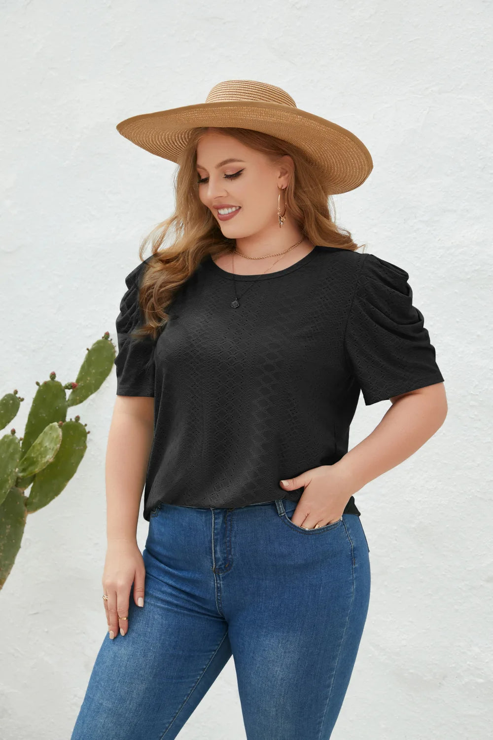 Frau mit Strohhut, schwarzem T-Shirt und blauer Jeans vor weißer Wand, Modefotografie.