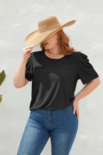 Frau mit schwarzem T-Shirt, blauer Jeans und Strohhut vor weißer Wand.