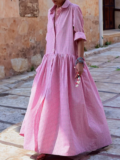 Frau in rosa kariertem Maxikleid auf gepflasterter Straße, Sommermode, lässiger Stil.