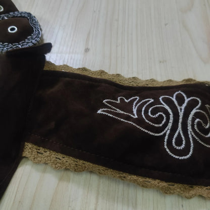 Brauner Ledergürtel mit weißer Stickerei und gehäkeltem Rand auf Holztisch.