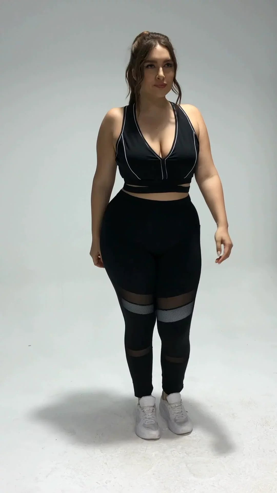 Frau in schwarzem Sport-BH und Leggings mit Netzdetails, Fitnessmode, Plus-Size, Studioaufnahme.