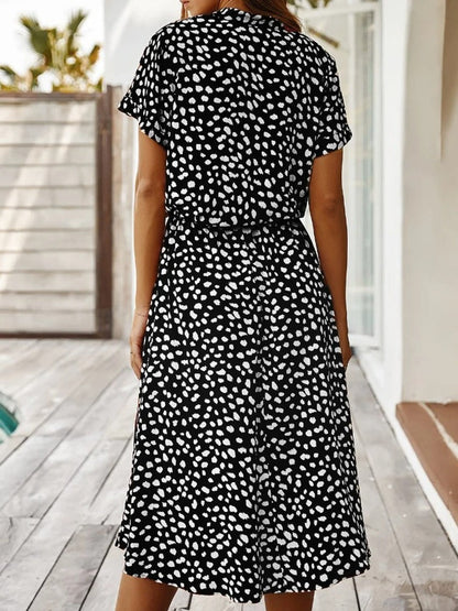 Frau in schwarz-weiß gepunktetem Sommerkleid auf Holzterrasse.