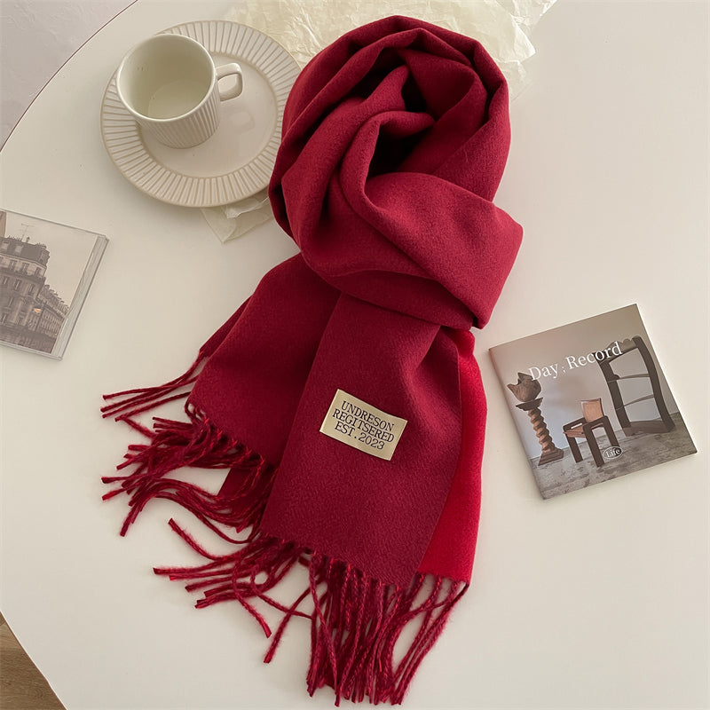 Roter Wollschal mit Fransen auf Tisch, neben Tasse und Magazinen, modisches Accessoire.