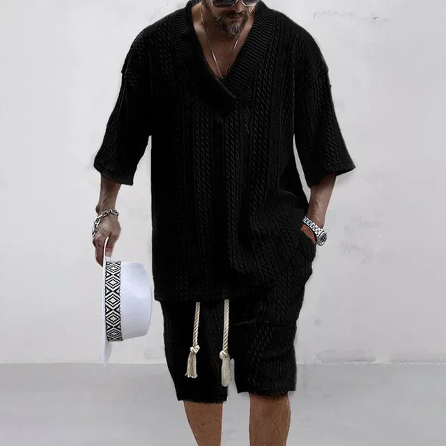 Mann in schwarzem Strickpullover und Shorts, hält weißen Hut, modisch, lässiger Stil.
