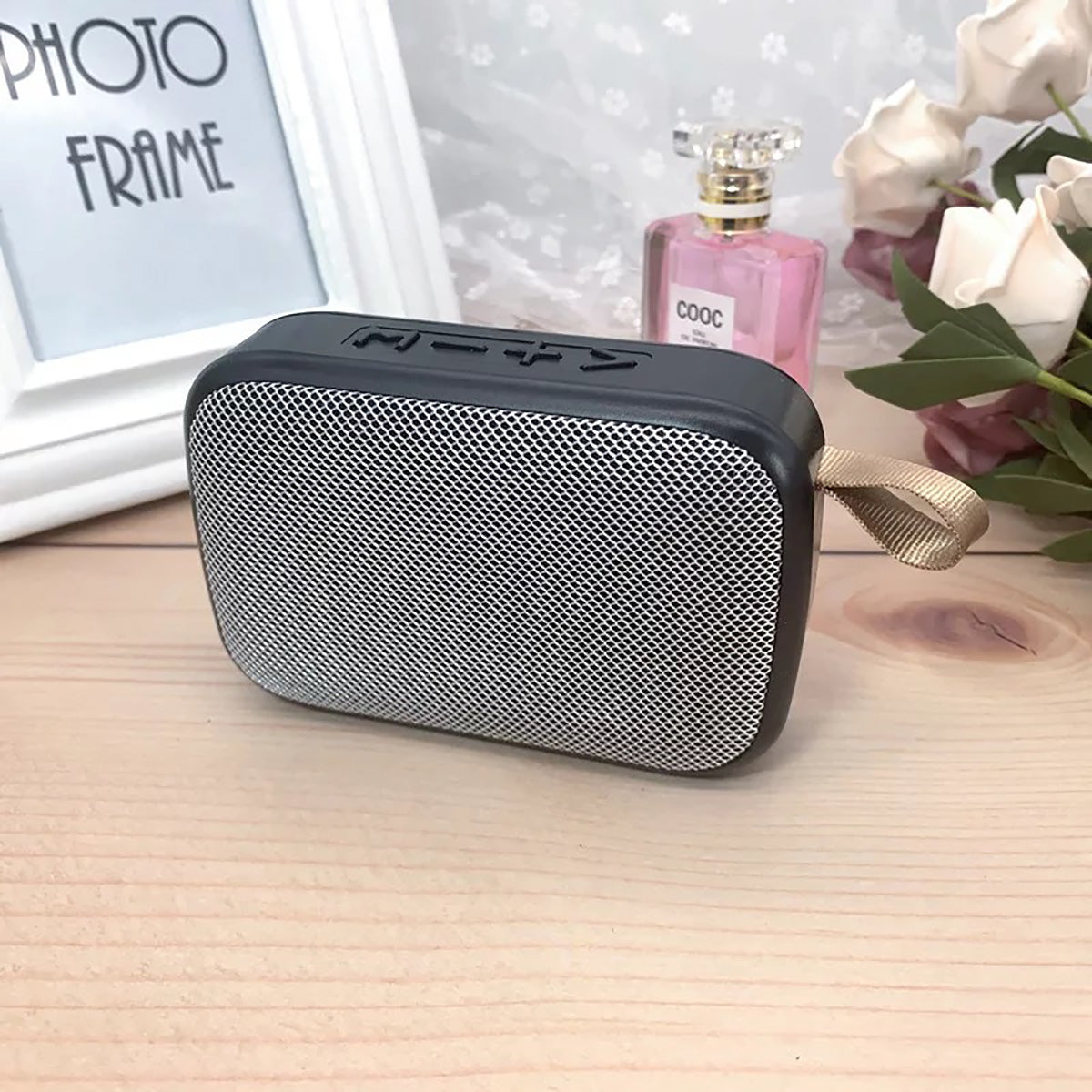 Tragbarer Bluetooth-Lautsprecher, schwarz-silber, mit Trageschlaufe, auf Holztisch.