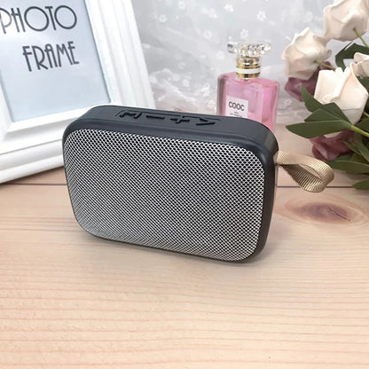 Tragbarer Bluetooth-Lautsprecher, schwarz-silber, mit Trageschlaufe, auf Holztisch.
