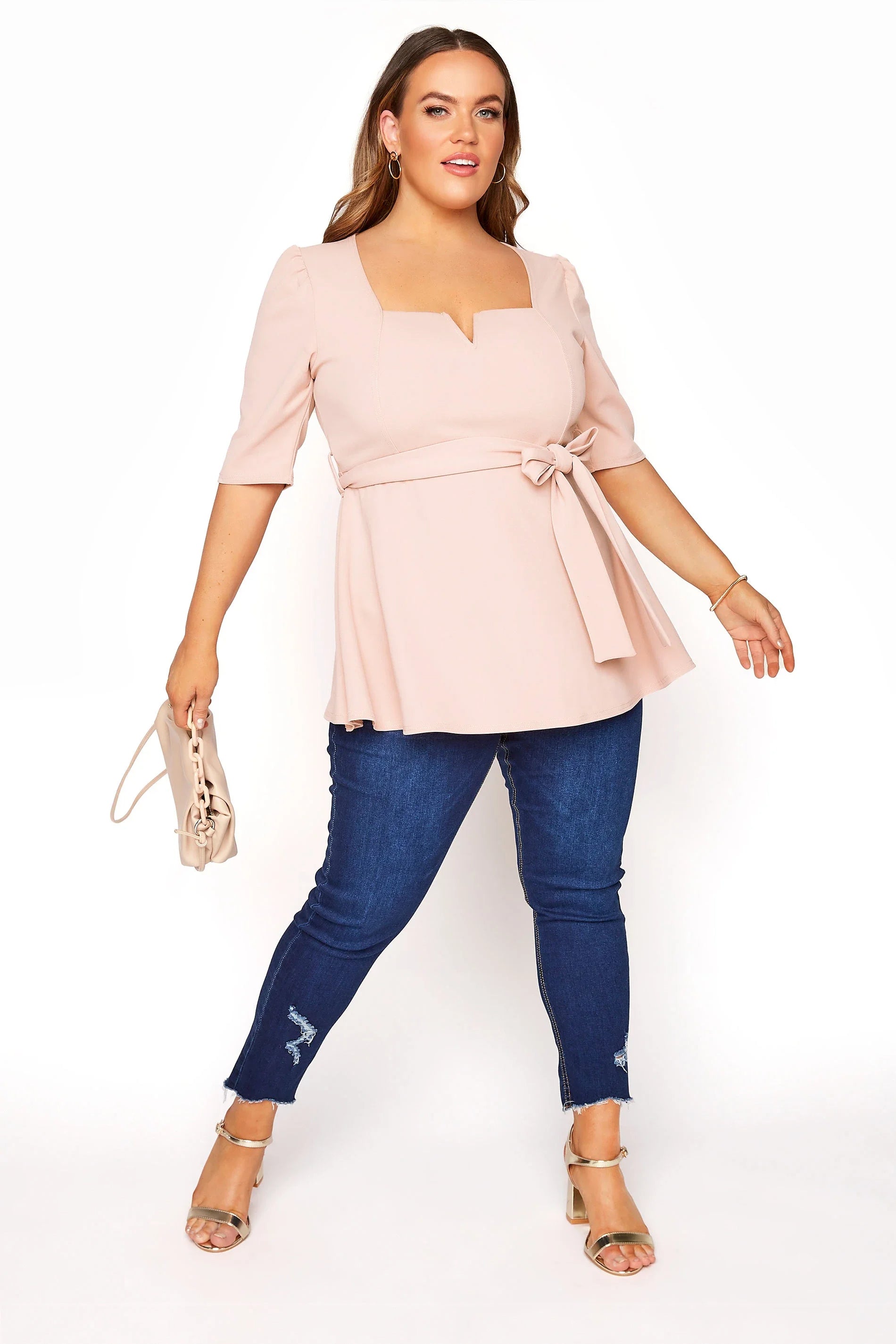 Frau in rosa Bluse mit Gürtel, blaue Jeans, Sandalen, Handtasche, Mode für große Größen.