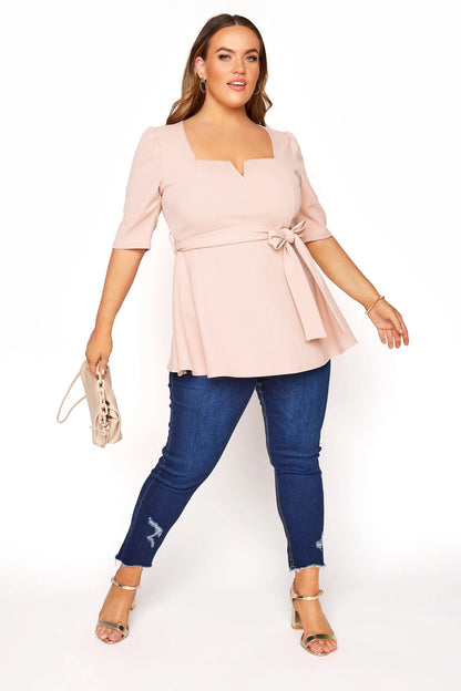 Frau in rosa Bluse mit Gürtel, blaue Jeans, Sandalen, Handtasche, Mode für große Größen.