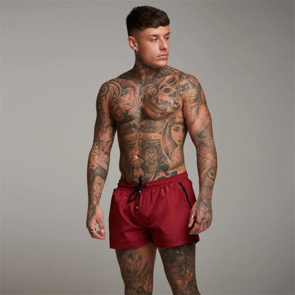 Mann mit Tattoos trägt rote Sportshorts, muskulös, Fitnessmode, Studioaufnahme.