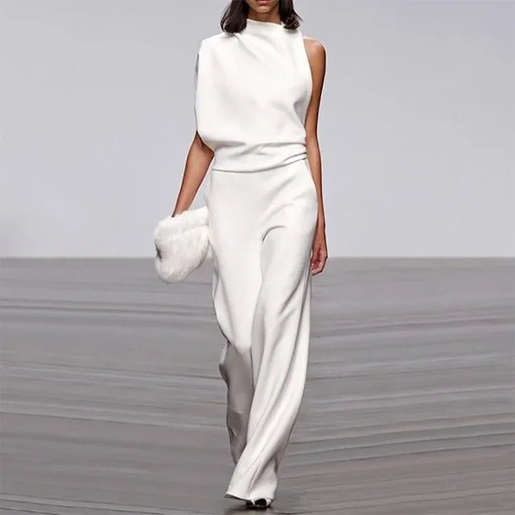 Frau in weißem, ärmellosem Jumpsuit mit asymmetrischem Schnitt und weißer Clutch auf Laufsteg.