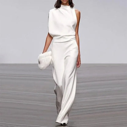 Frau in weißem, ärmellosem Jumpsuit mit asymmetrischem Schnitt und weißer Clutch auf Laufsteg.