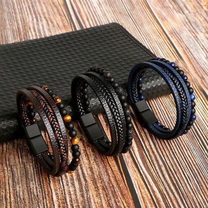 Drei geflochtene Lederarmbänder mit Perlen, schwarz, braun, blau, auf Holztisch.