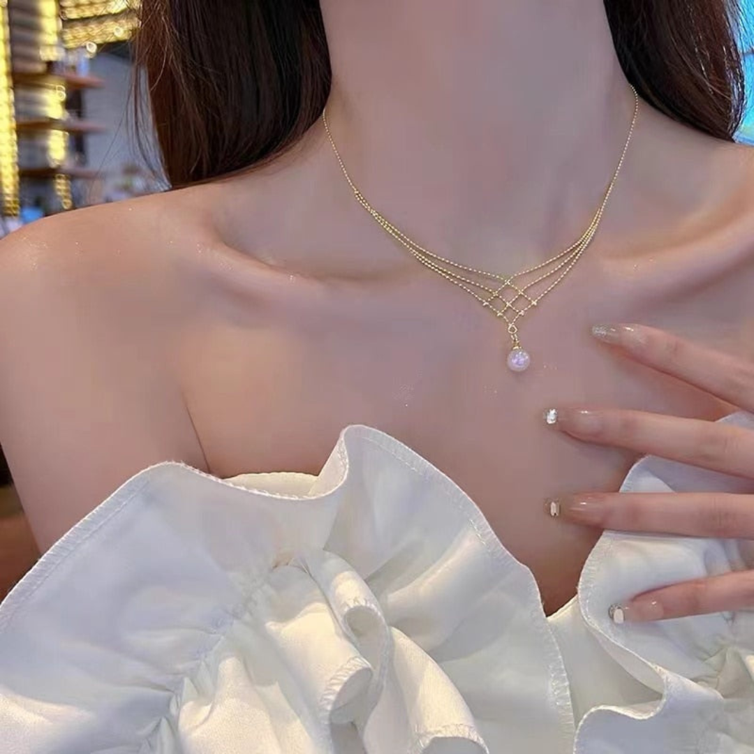 Frau mit goldener Halskette und Perlenanhänger, weißes Kleid, eleganter Schmuck, Nahaufnahme.
