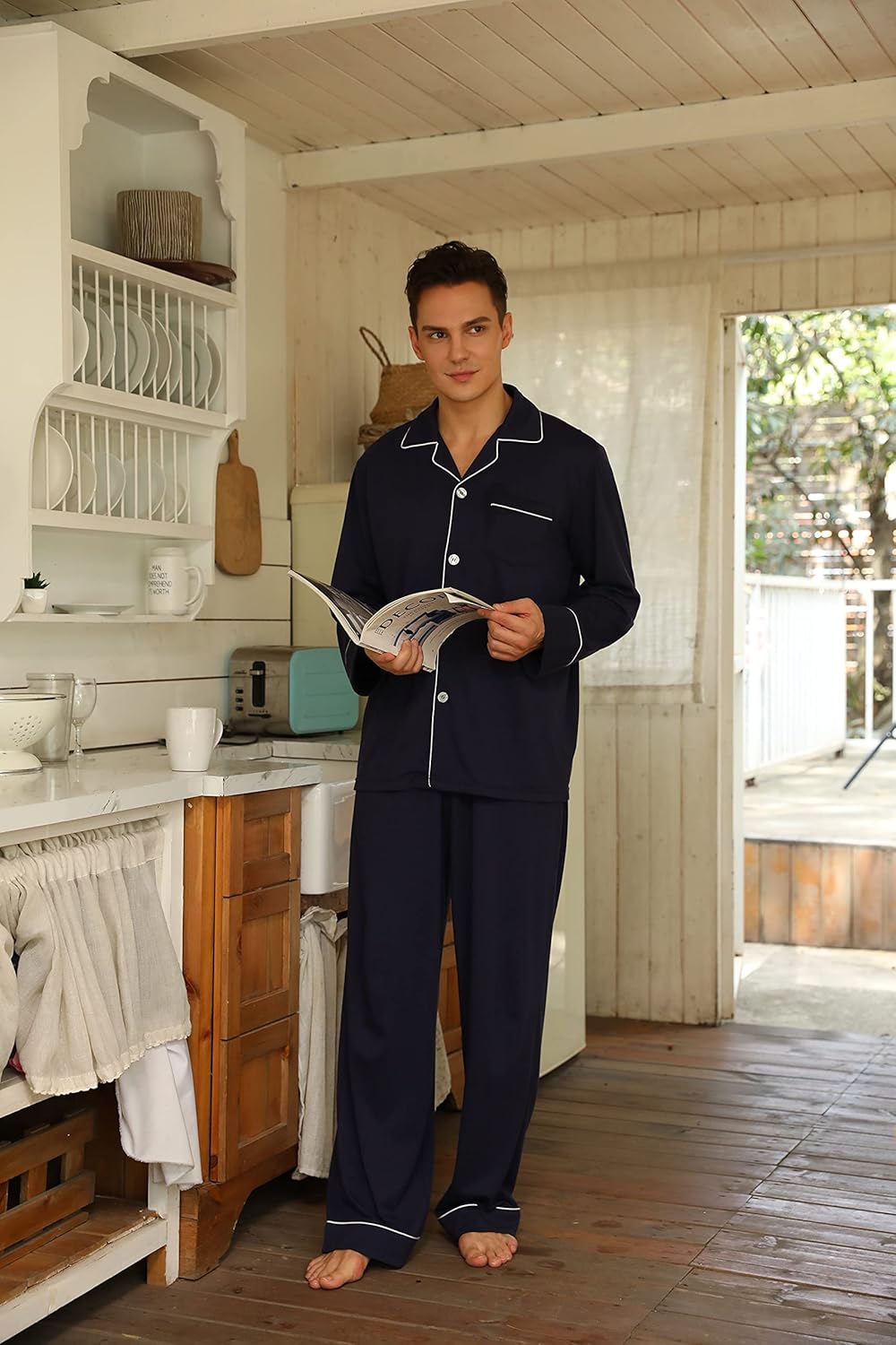 Mann in dunkelblauem Pyjama liest Zeitschrift in heller Küche, gemütliche Nachtwäsche.