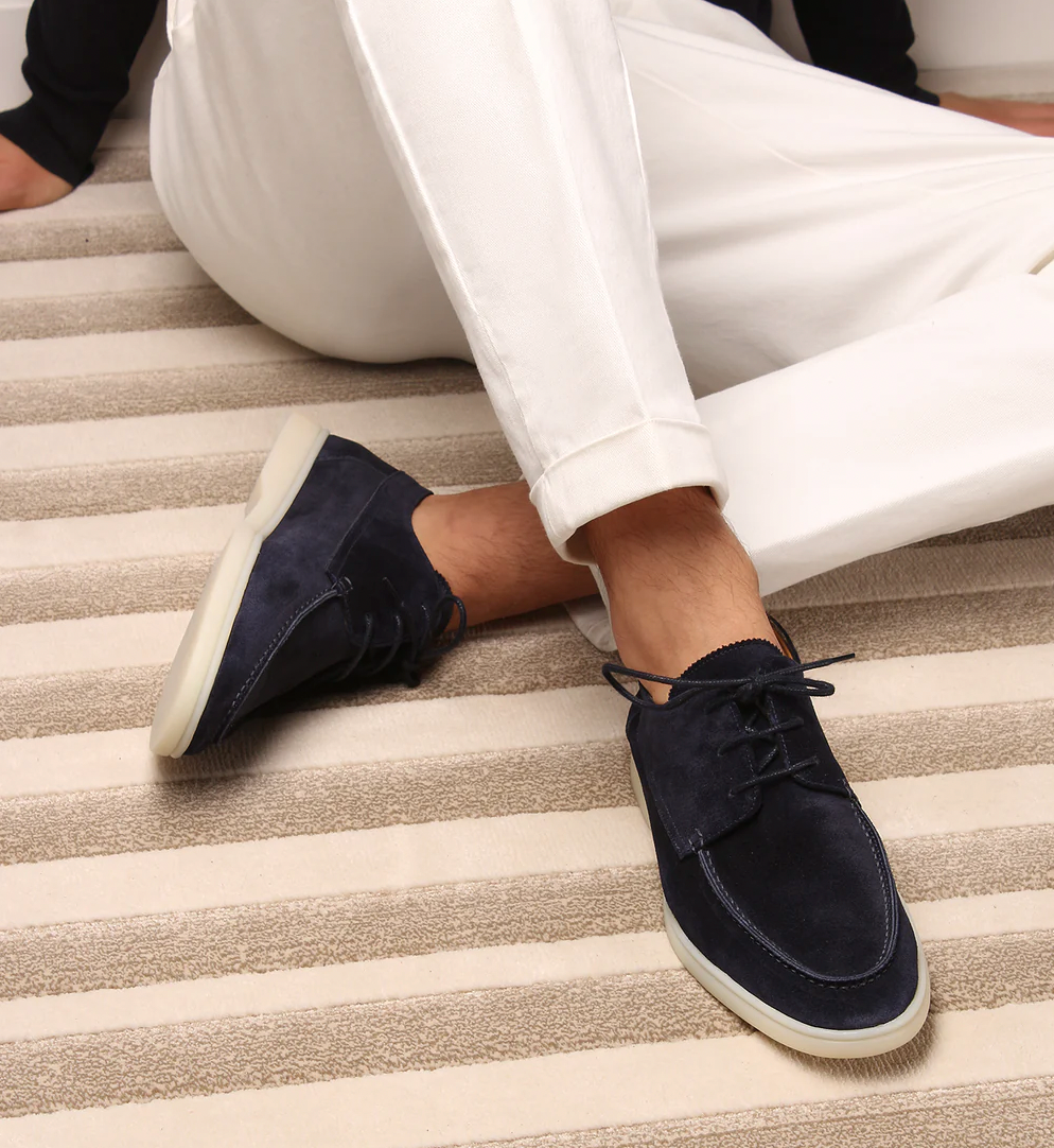 Dunkelblaue Wildleder-Sneaker für Herren, kombiniert mit weißen Hosen auf gestreiftem Teppich.